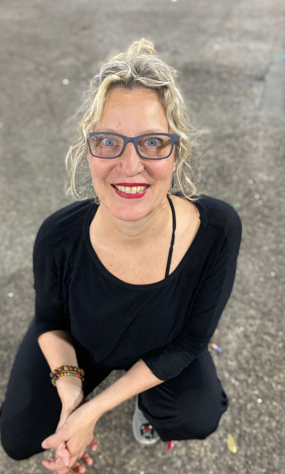 Mónica Ibáñez Fernández de Lis en cuclillas sobre el asfalto, vestida de negro, con gafas y las manos entrelazadas, sonriendo hacia la cámara